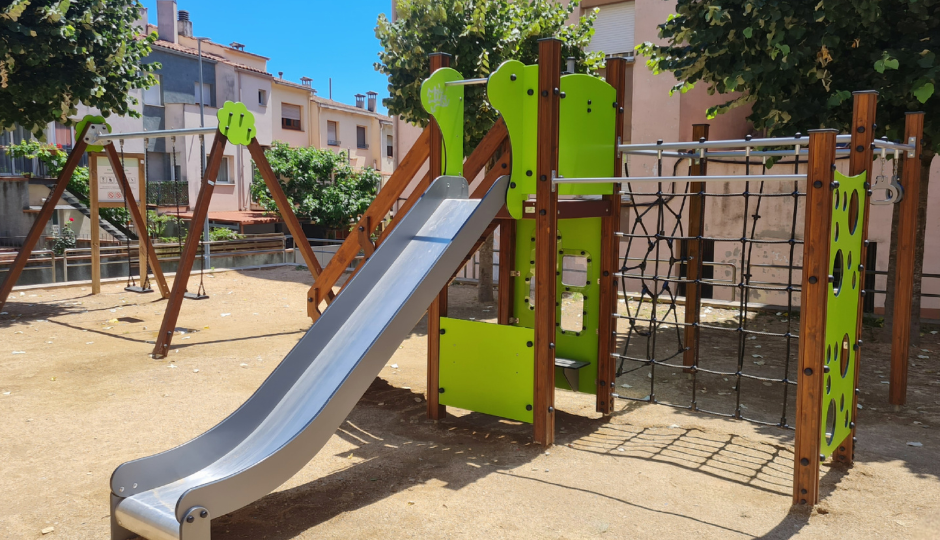 Parque infantil con estructura de madera tratada, tobogán metálico y redes para trepar, en un espacio urbano con árboles.