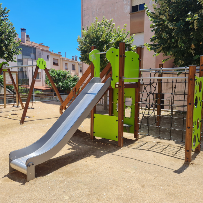 Parc infantil amb estructura de fusta tractada, tobogan metàl·lic i xarxes per grimpar, en un espai urbà amb arbres.